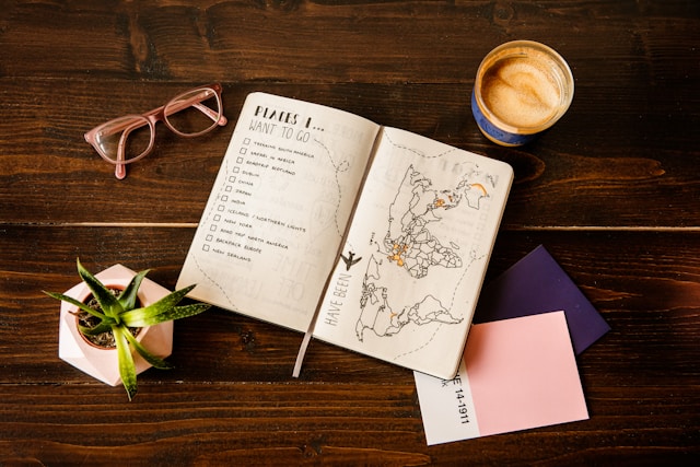 Een bullet journal met een lijst reisbestemmingen en een wereldkaart, naast een bril en koffie
